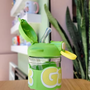 Green children's tumbler with straw on a wooden surface, blurred background
