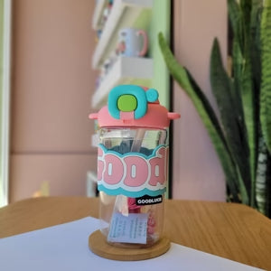 Bottle with colorful cap on a wooden surface with a plant in the background