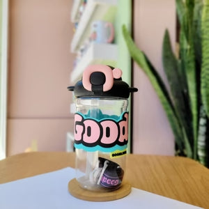 Clear bottle with black cap and colorful design on a wooden surface with a plant in the background