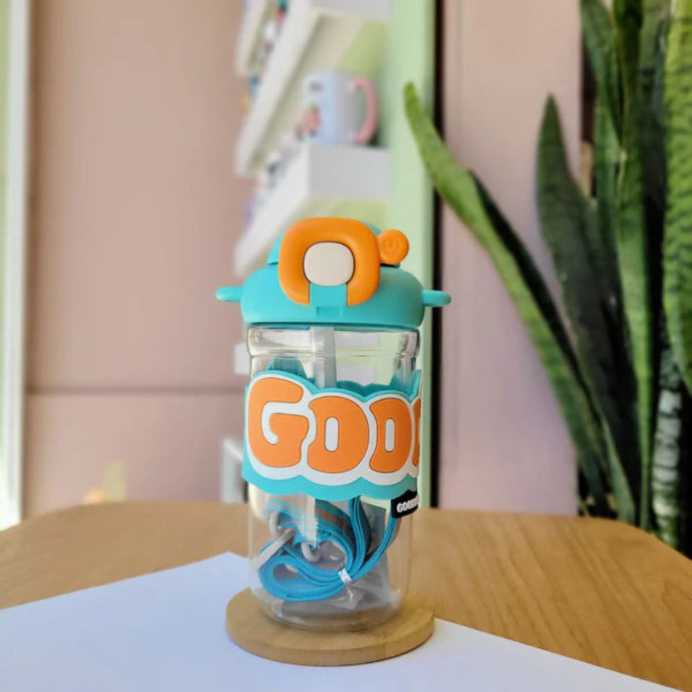 Clear tumbler with blue lid and handle, featuring the word 'GOOD' in orange letters, on a wooden surface.